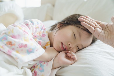 parent put the hand on forehead of sleeping toddler to check fever temperature while the kid got sickness in the bed.