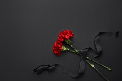 black funeral ribbon with carnation flowers on dark background