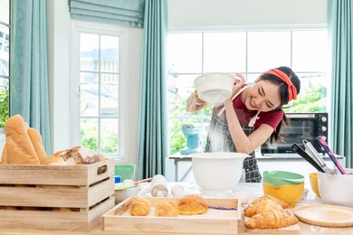 beautiful asian woman have fun sifting bread flour, preparing different ingredients before mixing, and kneading before baking in the oven to make homemade bread.