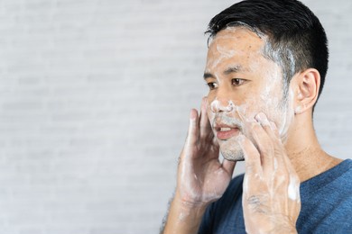 man using foam washing his face on gray background