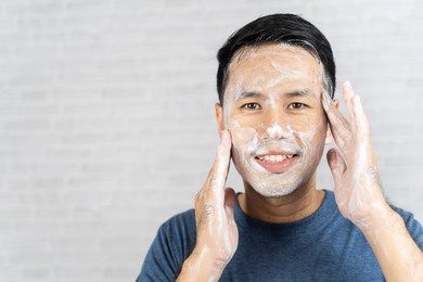 man using foam washing his face on gray background