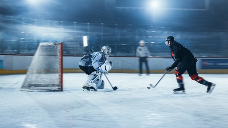 ice hockey rink arena: goalie is ready to defend score against forward player who shoots puck with stick. forwarder against goaltender one on one. tension moment with blurred motion.