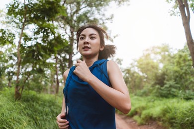 active young asian woman running at tropical forest trail. portrait female runner trail running in the forest. healthy lifestyle.