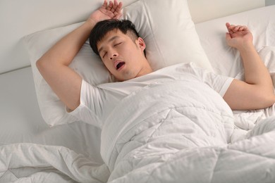 young asian man sleeping and snoring loudly lying in the bed