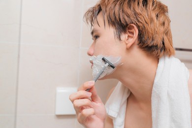 asian man shaving with foam looking in mirror