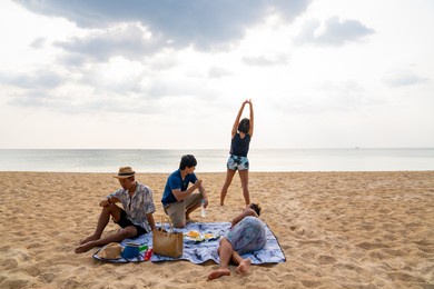 group of happy asian man and woman friends sitting on the beach enjoy picnic and talking together at summer sunset. male and female friendship relax and having fun summer outdoor lifestyle activity.