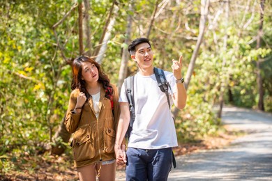 smiling young asian couple holding hands hiking and climbing together in forest. happy man with girlfriend relax and enjoy summer outdoor lifestyle with beautiful nature on holiday vacation travel.