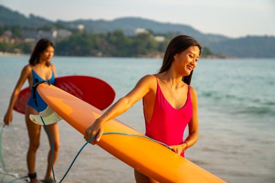 confidence asian woman girl friends in swimwear holding surfboard and walking together on the beach at summer sunset. female friendship enjoy outdoor activity lifestyle play extreme sports surfing