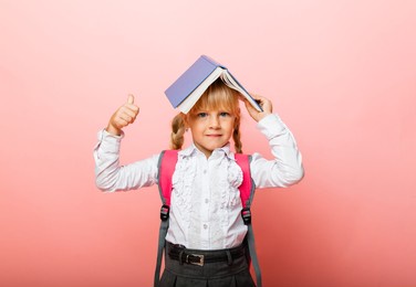 book roof over your head. little girl holding a textbook on her head. little girl reading a children's book on a pink background.