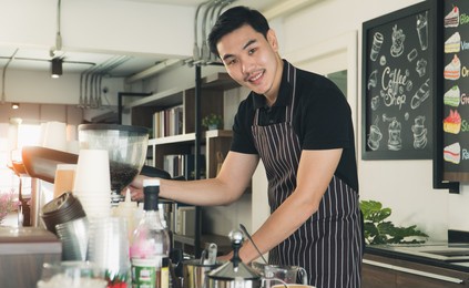young man asian small business owner coffee shop happy smiling confident proud optimistic at counter looking at camera. barista male wear apron preparing coffee and drink serve customers in cafe.