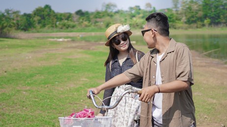 happy young asian couple walking bicycle in park in summer