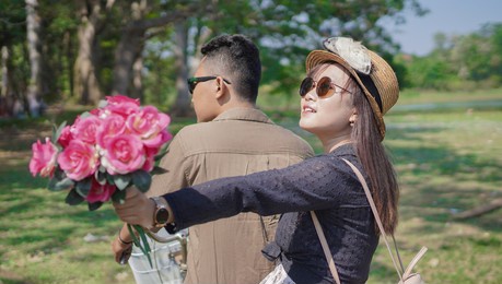 happy young asian couple cycling holding flowers in summer