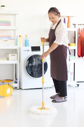 asian senior elderly woman housewife holding mop with plastic bucket, clean up floor mobbing in laundry room at home, grandma doing housework and cleaning clothes at house.