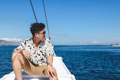 asian man wearing sunglasses and wireless earphone sitting on a boat while looking to the sea