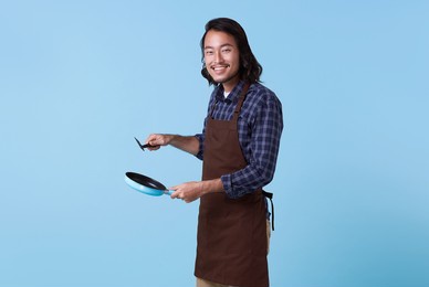 asian professional chief ready to cook, chef holding spatula and frying pan isolated on blue background.