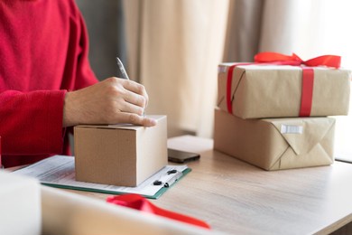close-up of male hands filling out a mailing form on a parcel box in the office or at home. small business owner preparing to send christmas presents. postal delivery and people. shipment concept.