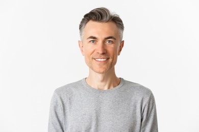 close-up of handsome middle-aged man in gray sweater, looking happy and hopeful, smiling at camera, standing over white background