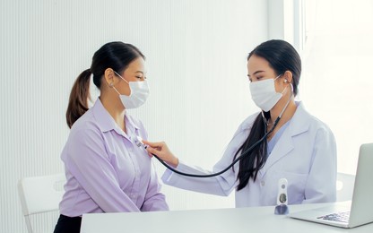 asian female doctor wearing face mask to protect virus, using stethoscope to listen heart beat of patient getting sick and health checking in hospital. medical concept