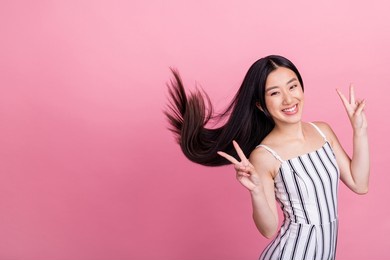 photo of adorable shiny young lady wear striped outfit showing v-signs empty space smiling isolated pink color background