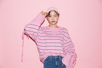 portrait of casual young asian woman with cap on pink background.