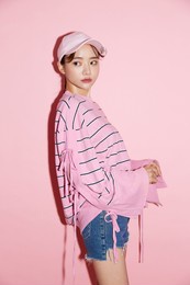 portrait of casual young asian woman with cap on pink background.