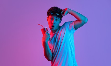 at cinema, movie. stylish young asian man isolated over lilac color studio background in pink neon light. concept of human emotions, facial expression, youth culture, diversity