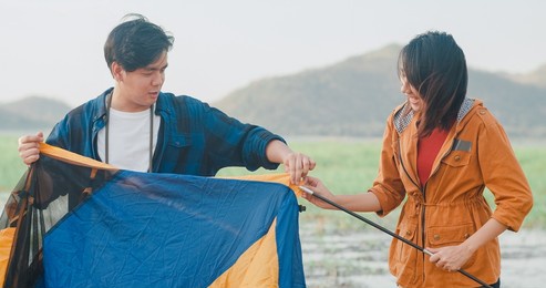 young asia campers couple setting up the tent camping gear outdoor near seaside. male and female travel having fun on a summer day at campsite. outdoor activity, adventure travel, or holiday vacation.