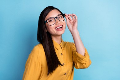 photo of young excited asian girl happy positive smile hand touch glasses isolated over blue color background