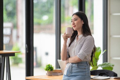beautiful businesswoman standing in the office while drinking her coffee
