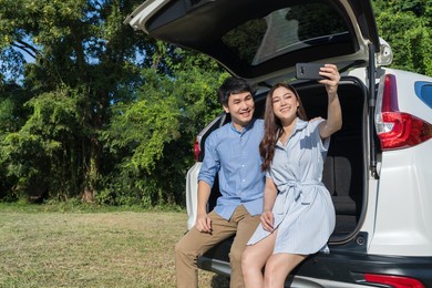 happy couple in love sitting and using smartphone taking a selfie in open car back