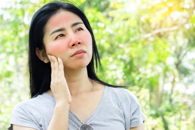asian woman having face skin problem with sunburn redness from ultraviolet of sunlight standing outdoors under sunny day 