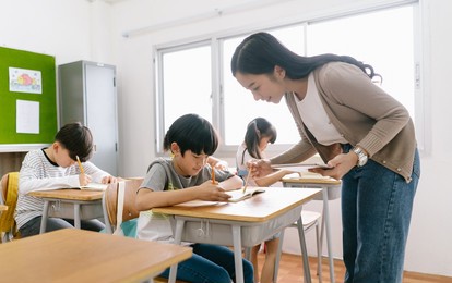 portriat of  asian female teacher helping elementary school boy in classroom at school. education, elementary school, learning concept.