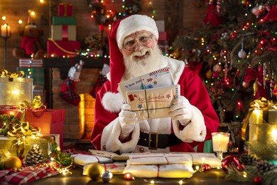 santa claus rejoicing with letters and mail in his post office indoors log cabin at the north pole. grandpa getting ready for christmas eve party. senior model with real beard cosplay father christmas