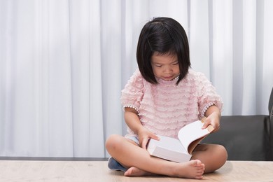 asian child sitting and reading big book on wood table in her house. happy girl sweet smile. kid was amazed by the new book she was holding. children aged 4-5 years old.