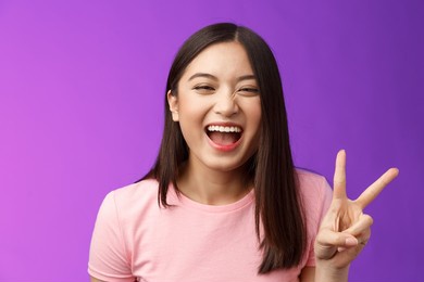 headshot sincere carefree laughing asian girl having fun, show peace victory sign, joyfully look camera, express enthusiasm and happiness, enjoy funny friendly company, stand purple background
