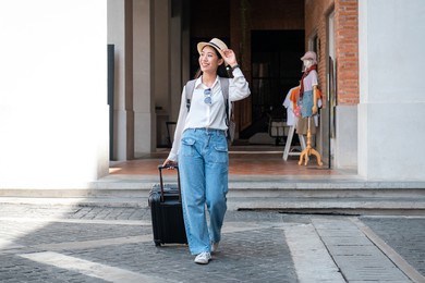 asian woman tourist is traveling on holiday trip with hat and dragging her black luggage while walking to passengers lounge in the airport