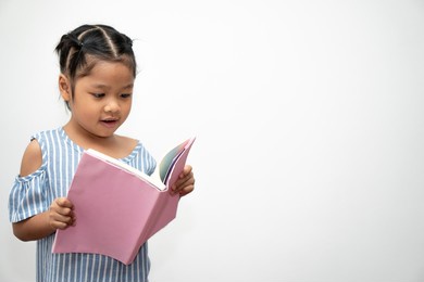 happy asian little preschool girl holding and read a book on white isolated background. concept of school kid and education in elementary and preschool