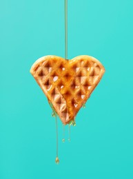 pouring maple syrup over one heart-shaped waffle against a green-colored background. close-up of maple syrup dripping on a waffle.