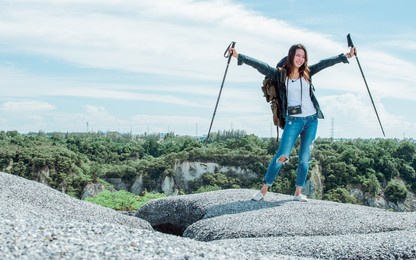 a beautiful asian woman with backpack climbing and standing on top of mountain with success. travel, vacation and summer concept