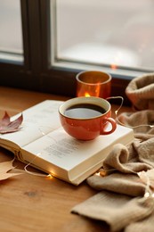 season, leisure and objects concept - cup of coffee, book, autumn leaves and candle on window sill at home