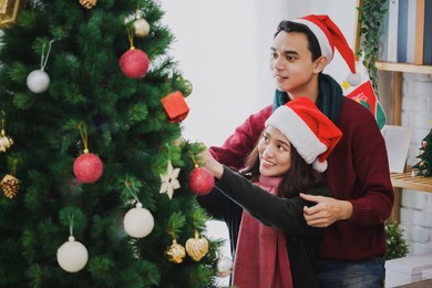 young asian couple decorating a christmas tree in christmas and happy new year holiday festival at home background.christmas celebration of lover concept.
