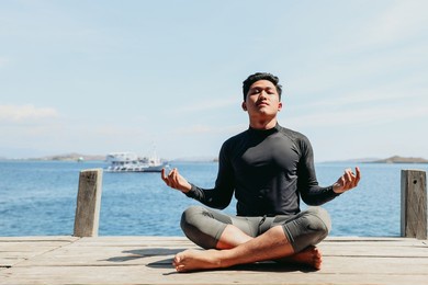 young asian man sitting in yoga position and meditating with sea background