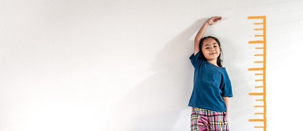 an adorable asian little child girl measuring the height growth with the orange drawing on the white wall background. girl power future and dream concept idea. copy space.