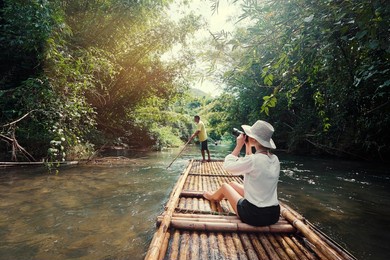 traveling by thailand. pretty young woman taking photo sailing jungle river on traditional bamboo raft.