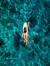 surfer girl rowing on surfboard in transparent turquoise ocean. aerial drone view with surfer woman