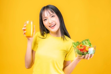 lifestyle beautiful beauty asian woman cute girl with bangs hair style in in yellow t shirt feel happy enjoy eating diet food fresh salad and orange juice for good health isolated on yellow background