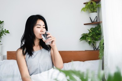 thirsty asian woman drinking water in bed after wake up in morning 