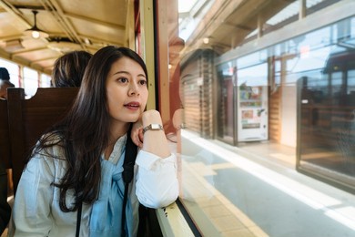 portrait of beautiful asian female visitor is looking at the station through the window while taking sagano romantic train in autumn in arashiyama kyoto, japan.