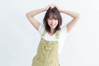 brunette long haired woman with curls touching head and smiling isolated on yellow