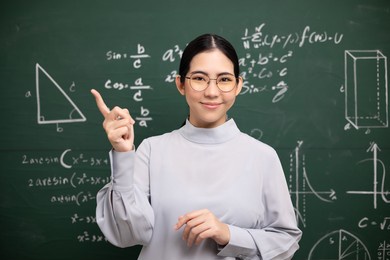 young asian teacher woman teaching standing showing index finger and video conference with student looking camera. female teacher training the mathematics in classroom blackboard from online course.